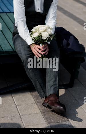 Eleganter Bräutigam in Hosen und Schuhen hält den Brautstrauß Stockfoto