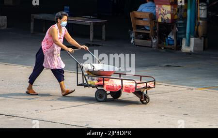 SAMUT PRAKAN, THAILAND, APR 07 2022, Eine Frau mit Schürze schiebt einen Wagen mit einer großen Pfanne Stockfoto