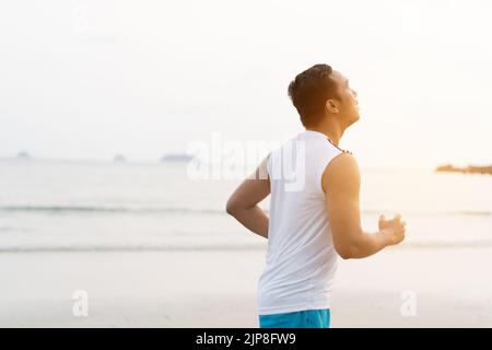 asiatischer Sportmann läuft am Meer. Laufen am Strand mit gesunden Beinen Körper, Hamstring Muskeln, Kniegelenk Gesundheit aktiver Lebensstil Panorama Stockfoto
