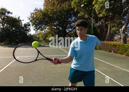 Biracial Mann spielt Tennis Rückkehr Ball über das Netz auf sonnigen Tennisplatz im Freien Stockfoto