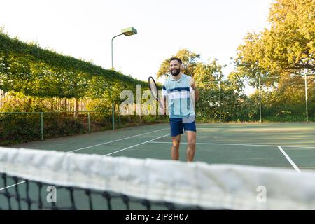 Fröhlicher Kaukasischer, der Tennis spielt und auf dem Tennisplatz im Freien feiert Stockfoto