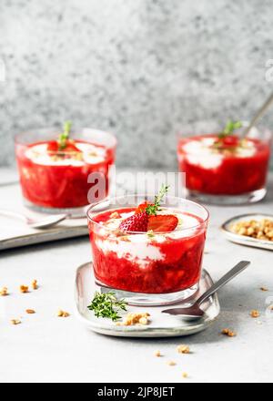 Süßes Erdbeerpüree und Frischkäse-Dessert mit frischen Beeren, Müsli und Thymian-Zweig in Gläsern dekoriert. Hausgemachtes gesundes Lebensmittelkonzept. Stockfoto
