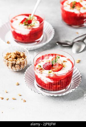 Gesundes Sommer-Frischkäse-Dessert mit Erdbeerpüree, frischen Beeren, Müsli und Thymian-Zweig in Glasschüsseln. Vegan gesundes Frühstück. Hausgemacht Stockfoto