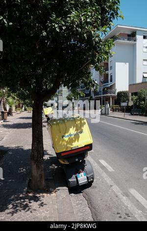 Das Motorrad Poste Italiane parkt unter einem Baum unter der Mittagssonne, damit der Sitz und der Lenker nicht zu heiß werden. Stockfoto