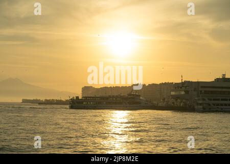 Izmir, Karsiyaka, Türkei - 5. November 2021: Fähre nähert sich dem Pier bei Sonnenuntergang. Izmir, Pier von Karşıyaka in der Ägäis. Stockfoto