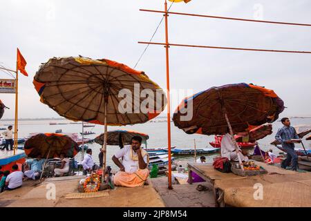 Priester, der unter einem riesigen Regenschirm bei Dashashwamedh Ghat am Ganga-Fluss Ganges sitzt, Varanasi, Banaras, Benaras, Kashi, Uttar Pradesh, Indien Stockfoto
