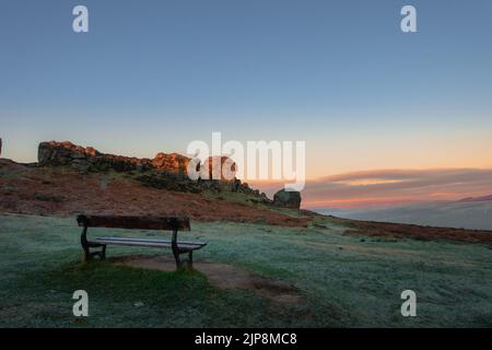 Landschaften in Großbritannien: Die perfekte Bank, um die goldene Stunde zu genießen und den Sonnenaufgang über den Cow and Calf Rocks, Ilkley Moor, England, zu beobachten. Stockfoto