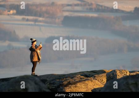 Frau im Winter, die Fotos vom Sonnenaufgang von Ilkley Moor aus gemacht hat. West Yorkshire, England Stockfoto