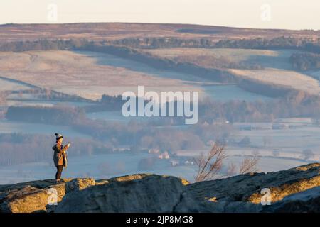 Frau im Winter, die Fotos vom Sonnenaufgang von Ilkley Moor aus gemacht hat. West Yorkshire, England Stockfoto