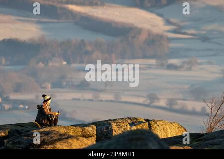 Frau im Winter, die die Wärme der Sonne bei Sonnenaufgang von Ilkley Moor genießt. West Yorkshire, England Stockfoto