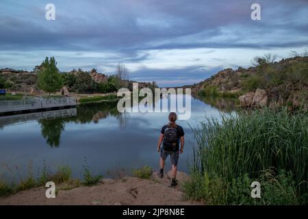 Ein kaukasischer Wanderer, der die Aussicht auf den Fain Lake nach Sonnenuntergang im Prescott Valley, Arizona, bewundert Stockfoto