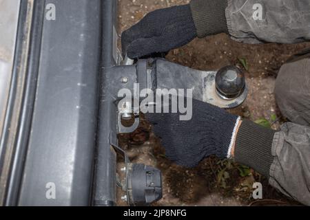 Ein Mann installiert einen eisernen Anhängerhaken an einem Anhängerfahrzeug. Gerät für den Transport. Stockfoto