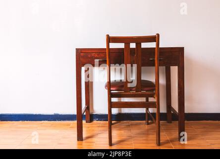 Schöner Vintage Holztisch und Stuhl, Rückansicht von Tisch und Stuhl, Tisch und Stuhl in weißer Zimmerwand und braunem Boden, keine Menschen, natura Stockfoto