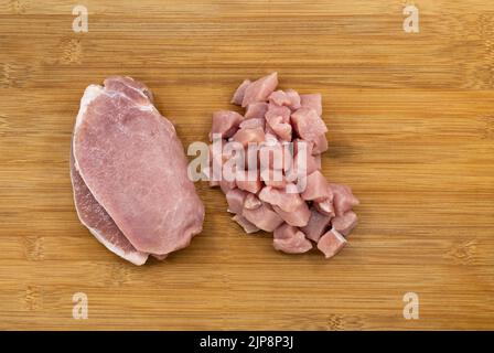 Draufsicht frisches Schweinefilet und Haufen würfelgeschnittenes Schweinefleisch auf Bambus-Holzbrett. Zwei verschiedene Arten von frischem Schweinefleisch geschnitten. Stockfoto