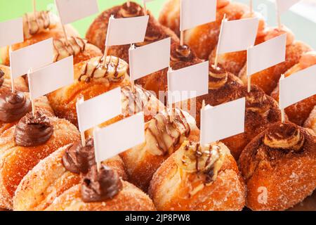 Weiße Dummy-Flaggen auf einer Vielzahl von Bombolon-Donuts, die frisch in einer Bäckerei hergestellt werden. Stockfoto