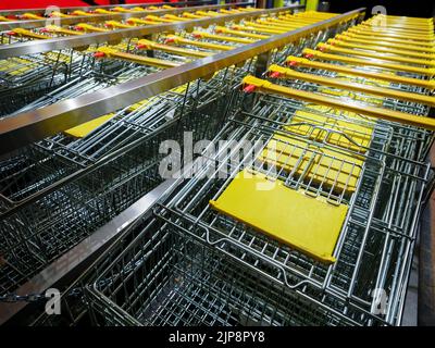 Reihe gestapelter Trolley-Wagen aus Metall mit gelben Griffen in der Nähe des Supermarkts Stockfoto