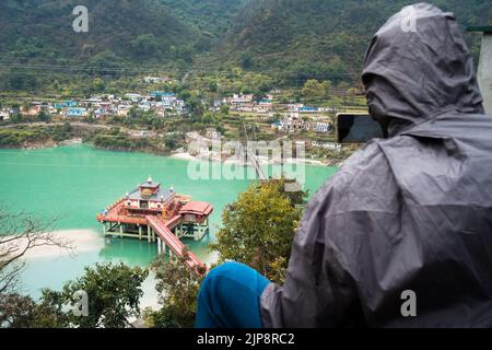 Januar 24. 2022, Srinagar Uttarakhand Indien. Ein männlicher Tourist mit einem Rucksack, der ein Foto des Dhari Devi hinduTemple am Ufer von Al fotografiert Stockfoto