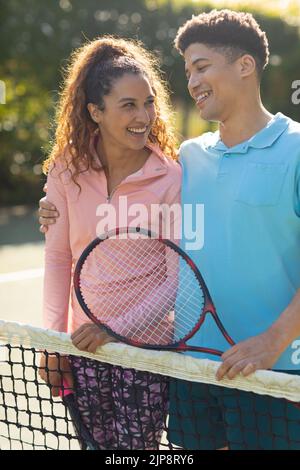 Vertikales Bild eines glücklichen, vielfältigen Paares, das auf dem Tennisplatz läuft und spricht Stockfoto