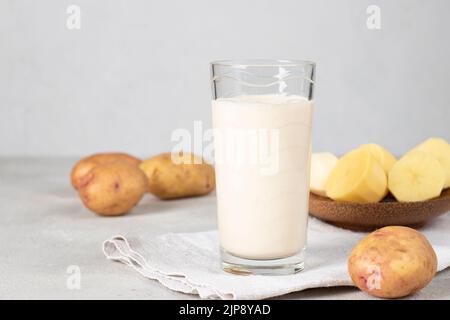 Vegane Kartoffelmilch im Glas und Kartoffel in Teller auf grauem Hintergrund. Milchaustauschstoff auf pflanzlicher Basis und laktosefrei Stockfoto