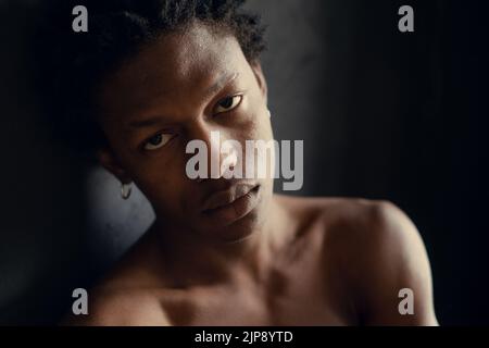 Junger afroamerikanischer Mann mit ernstem Ausdruck auf schwarzem Hintergrund Stockfoto