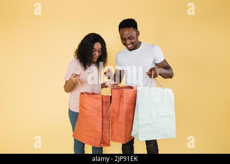 Aufgeregte afroamerikanische Frau und Mann schauen sich die Kamera an und halten Einkaufstaschen. Glücklich lockig Mädchen und Kerl in lässigen Kleidung glücklich, dass die Käufe. Stockfoto