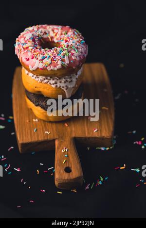 Köstliche Donuts auf Holzbrett, auf Holzschneidebrett auf schwarzem Hintergrund platziert. Stockfoto