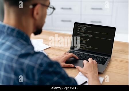 Foto eines Programmierers mit Laptop. Blick über die Schulter eines Mannes, eines IT-Spezialisten auf einen Laptop-Bildschirm, ein männlicher Programmierer schreibt Codes für eine Anwendung vor, entwickelt Software. IT-Technologie Stockfoto
