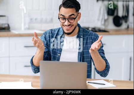 Staunender arabischer oder indischer Mann mit Brille, cleverer Student oder Freiberufler mit gemischter Rasse, Fernkommunikation per Videoanruf per Laptop, Online-Webinar anhören, Vortrag, lächelnd freundlich Stockfoto