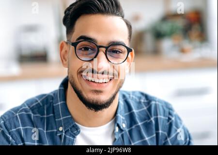 Nahaufnahme eines hübschen attraktiven jungen Mannes mit Brille, Freiberufler oder Student, in einem legeren Hemd, mit perfekten weißen Zähnen, der mit einem fröhlichen Lächeln auf die Kamera blickt Stockfoto