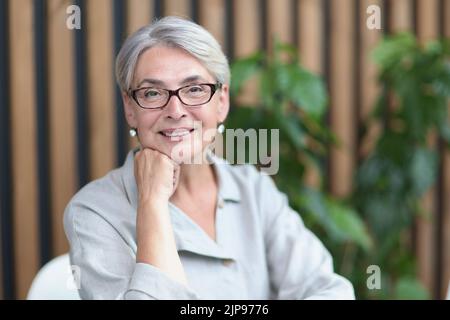 Lächelnde 60-jährige Geschäftsfrau, die im Büro einen Computer benutzt Stockfoto