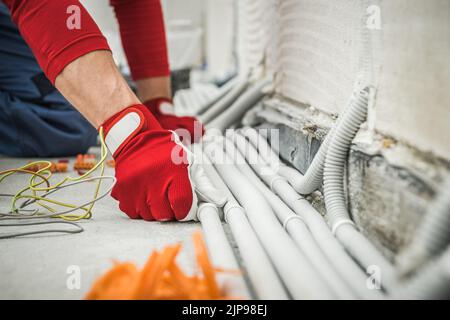 Nahaufnahme der Hände eines Elektrikers in roten Schutzhandschuhen zur Überprüfung der Installation von Kunststoffleitungen von Elektrokabeln in Wohngebäuden. Industrie Stockfoto