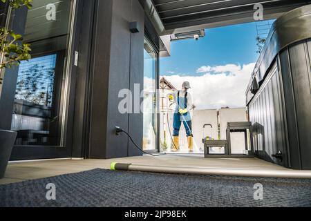Kaukasischer Mann in seiner 40s Reinigung der Außenterrasse seines Hauses mit Druckwascher. Vorbereitungen vor Beginn der Sommersaison. Home und Stockfoto