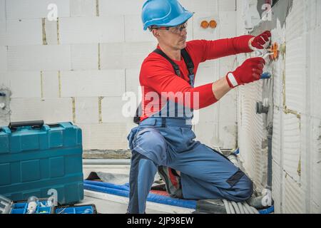 Installation der elektrischen Anlage in einem frisch erbauten Wohnhaus. Kaukasischer Arbeiter, der Steckdosen an der Wand anführt. Industriedesign. Stockfoto