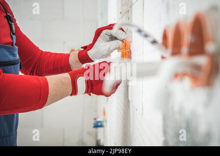Elektriker in Arbeitsschutzhandschuhe zur Befestigung von Steckdosen in der Wand. Nahaufnahme Der Seitenansicht. Industriedesign. Stockfoto