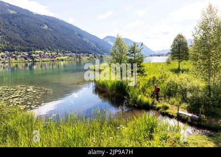 Radfahrerin auf einer Fahrradtour mit Blick auf den wunderschönen Weissensee in Kärnten in Österreich Stockfoto