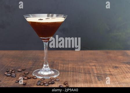 Glas Espresso martini mit Kaffeebohnen auf Holztisch und schwarzem Hintergrund Stockfoto