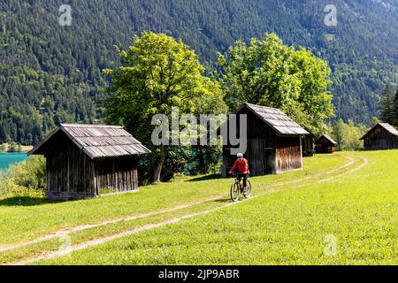 Radfahrerin inmitten traditioneller Holzhütten auf einem Fahrradausflug zum wunderschönen Weissensee in Kärnten in Österreich Stockfoto