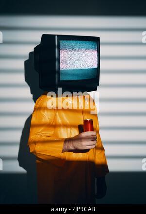 Surreale Kunst des fernsehsüchtigen Mannes mit Fernsehen statt Kopf. Medien Zombie-Konzept mit Männchen in leuchtend gelben Regenmantel mit süßen Soda in einem roten c Stockfoto