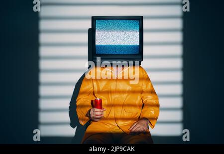 Surreale Kunst des fernsehsüchtigen Mannes mit Fernsehen statt Kopf. Medien Zombie-Konzept mit Männchen in leuchtend gelben Regenmantel mit süßen Soda in einem roten c Stockfoto