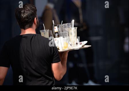 Hamburg, Deutschland. 16. August 2022. Ein Kellner im Alsterarkaden trägt ein Tablett mit gebrauchten Gläsern und leeren Flaschen. Quelle: Jonas Walzberg/dpa/Alamy Live News
