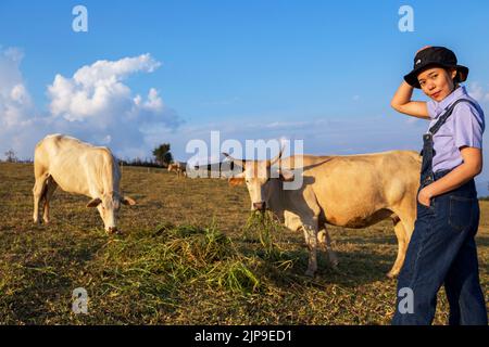 asiatische Frau in Cowboy Mode-Stil entspannen ihren Urlaub mit Kühen Familie gibt Weideplatz und bunte Natur Hintergrund Stockfoto