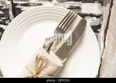 Vintage alte Gabel und Messer in einer Serviette gehüllt liegen auf einem weißen Teller auf grauem Hintergrund, WortschDienst, Besteck Stockfoto