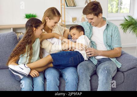 Glückliche Eltern und Kinder kitzeln sich gegenseitig, während sie zu Hause auf dem Sofa sitzen. Stockfoto