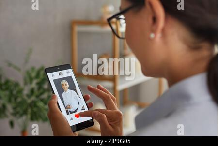 Frau, die Liebe sucht, scrollt durch Profile von Männern in Dating-Anwendung auf Handy. Stockfoto