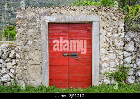 Steinmauer mit frisch lackierter roter Holztür, Cres (Kroatien) Stockfoto