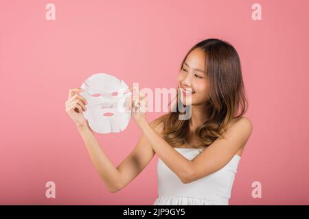 Gesundheitszentrum. Asiatische Frau hält reinigende Maske Gesicht auf den Händen, Portrait schön weiblich lächelnd hält Gesichtsmaske, Studio Schuss isoliert auf b Stockfoto