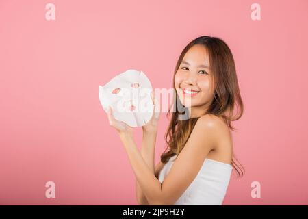 Gesundheitszentrum. Asiatische Frau hält reinigende Maske Gesicht auf den Händen, Portrait schön weiblich lächelnd hält Gesichtsmaske, Studio Schuss isoliert auf b Stockfoto