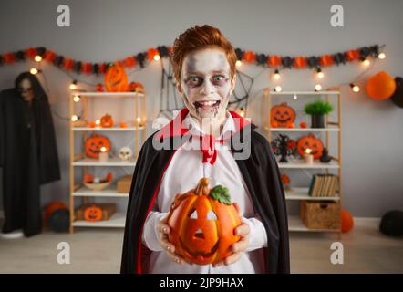 Kind in einem gruseligen Halloween Vampir Kostüm gekleidet, das seine Jack-o-Laterne hält Stockfoto