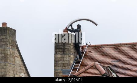 Installation eines flexiblen Stahlrauchabgasklappes in einen Kamin während einer Holzofeninstallation, Großbritannien Stockfoto