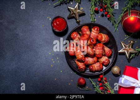 Traditionelles Weihnachtsgericht Rezept Schweine in Decken, Würstchen in Speck eingewickelt, im Ofen gebackenes Blätterteig Hot Dogs Rollen mit Weihnachtsbaum Ästen, decorati Stockfoto